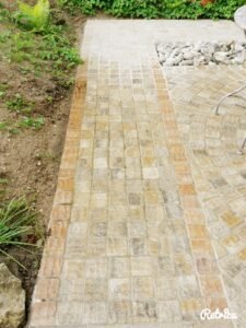 Fachgerecht ausgeführte Pflasterarbeiten: Ein gerader Gartenweg mit sauberer Randbegrenzung schließt an ein Rundpflaster-Element an. Die farblichen Akzente der Einfassung betonen die Wegeführung.