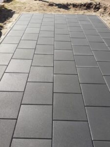 Nahaufnahme einer präzise verlegten Pflasterfläche: Sauberes Fugenbild und perfekt ausgerichtete anthrazitfarbene Steinplatten auf einer vorbereiteten Baustelle.